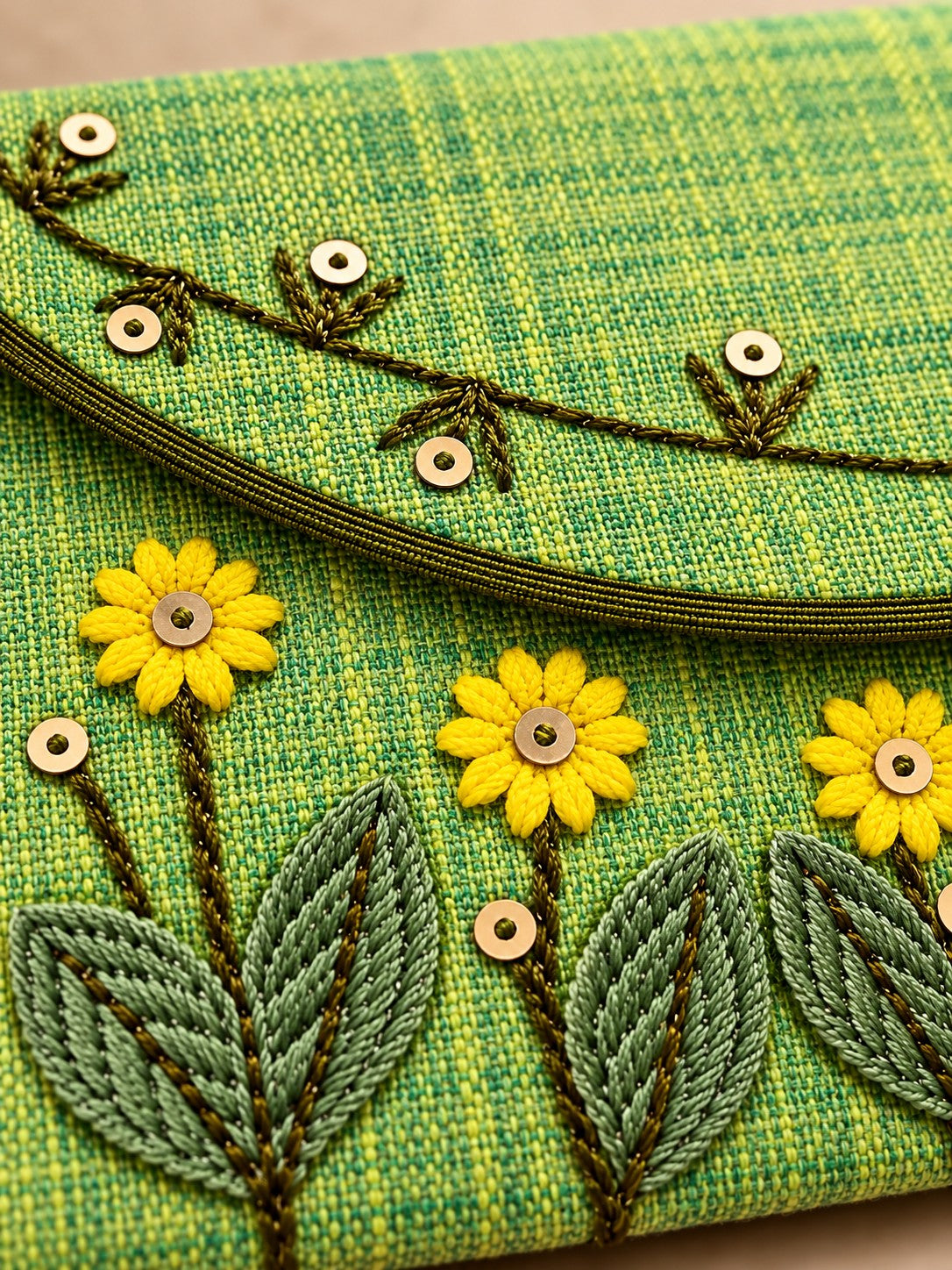 Close-up of hand embroidered yellow flowers and sequins on green Khadi envelope